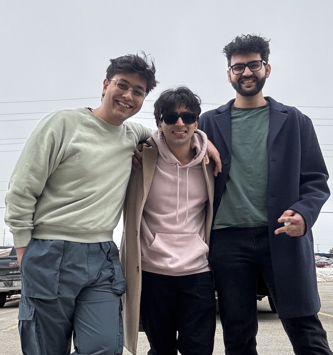 Teja, Aasees and Lakshit, the three ImpulsTrip founders, standing arm in arm in a parking lot on an overcast day.